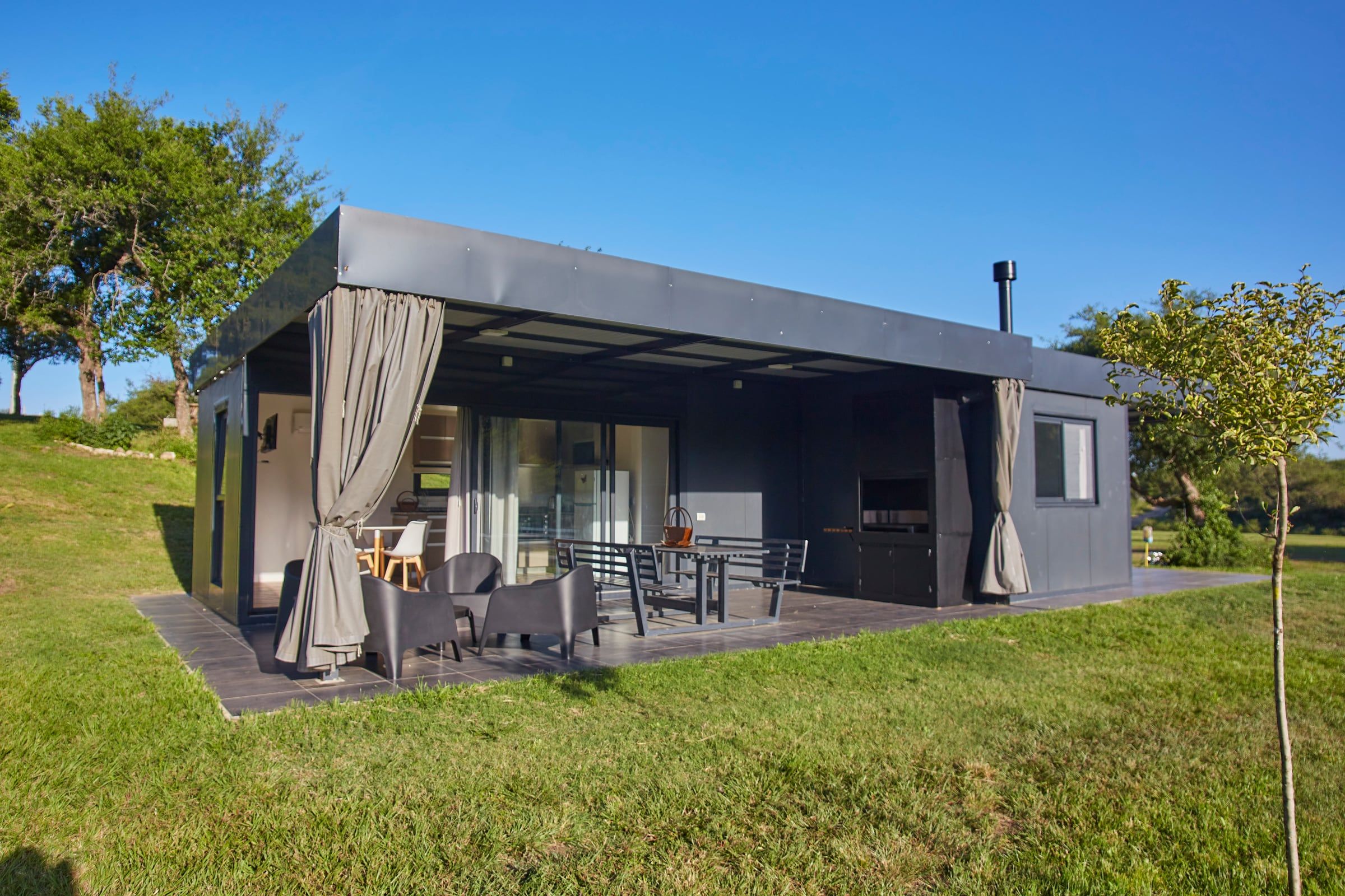 Cabaña de líneas modernas con galería, cortinas y parque alrededor