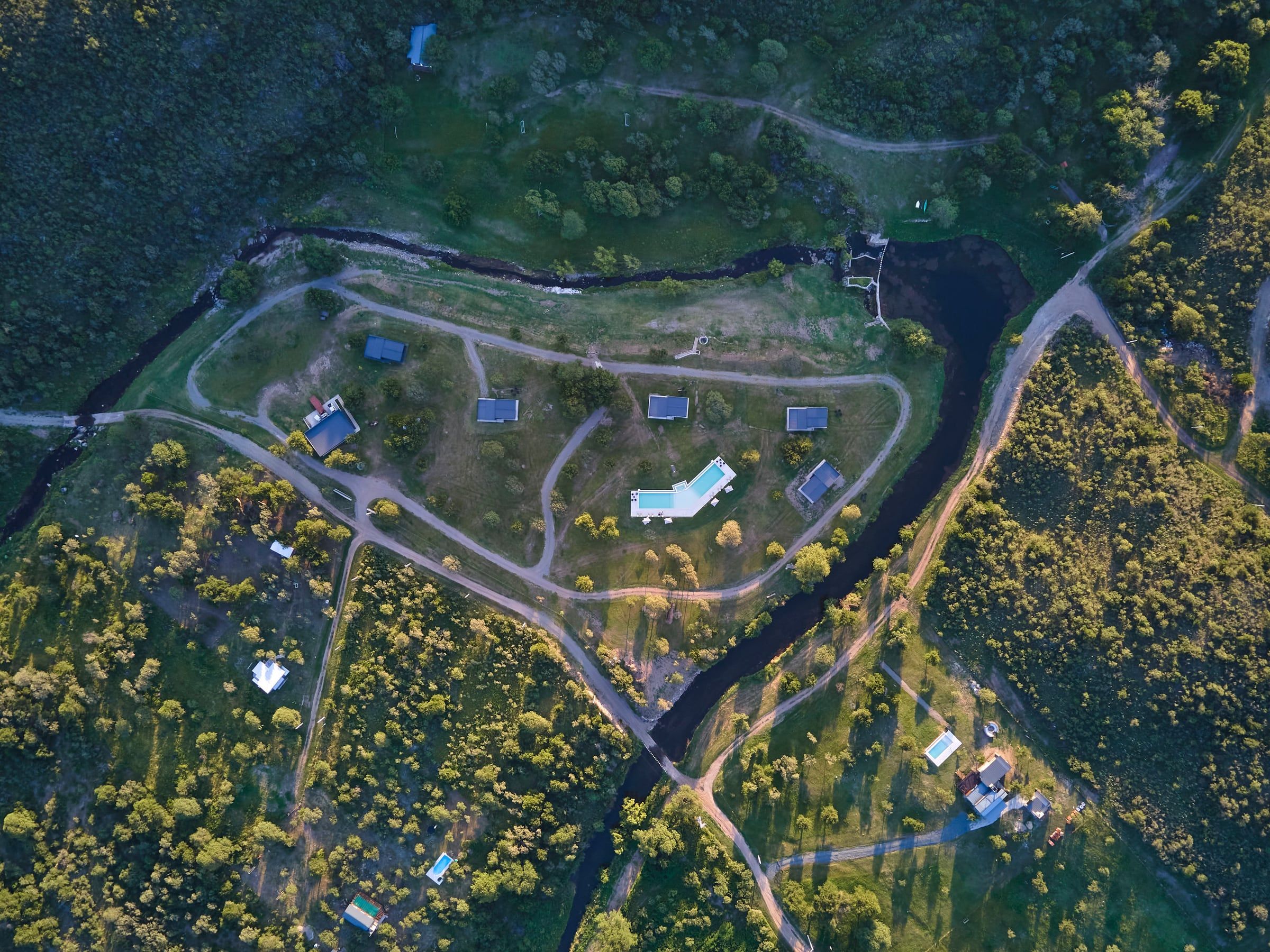 Vista aérea del predio: el arroyo rodea las cabañas y la pileta