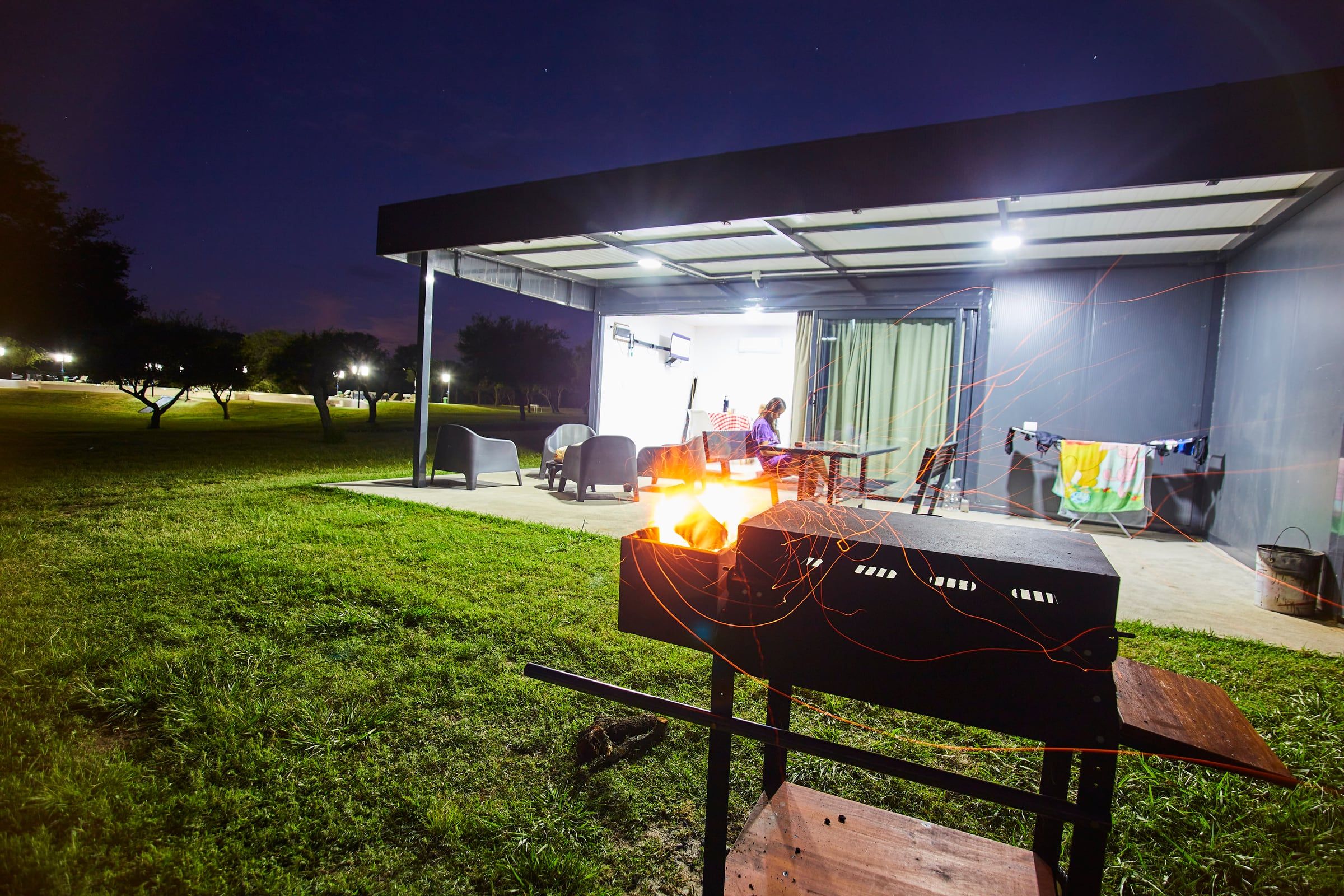 Galería iluminada de noche, con un brasero encendido en el pasto